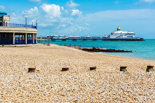 Am Pier von Eastbourne erwartet Urlauber ein sonniger Kiesstrand an Englands Küste.